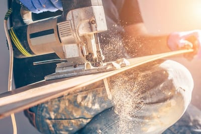 Worker Using Electric Jigsaw to Cut a Board of Wood