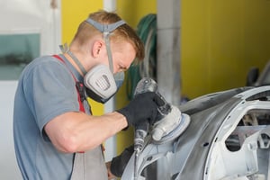 Man sanding car bumper and wearing a mask to avoid inhalation of metalworking dust